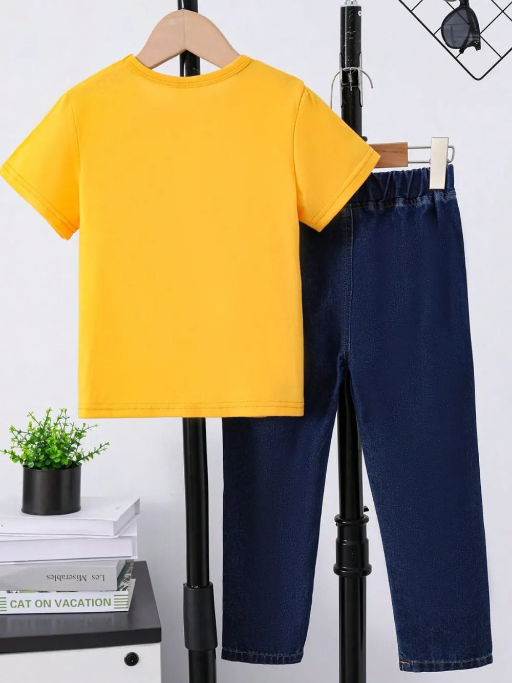Yellow t-shirt and navy pants displayed on a rack with a small green plant nearby.