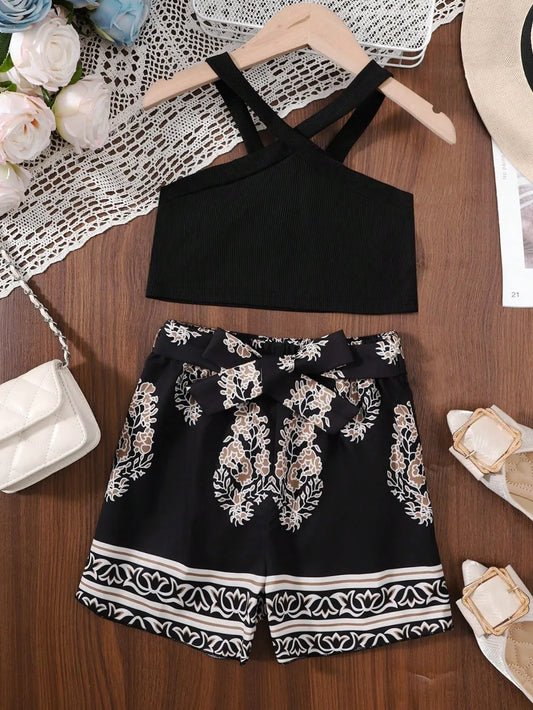 Black crisscross crop top with floral patterned shorts, white handbag, and sandals on a wooden surface.