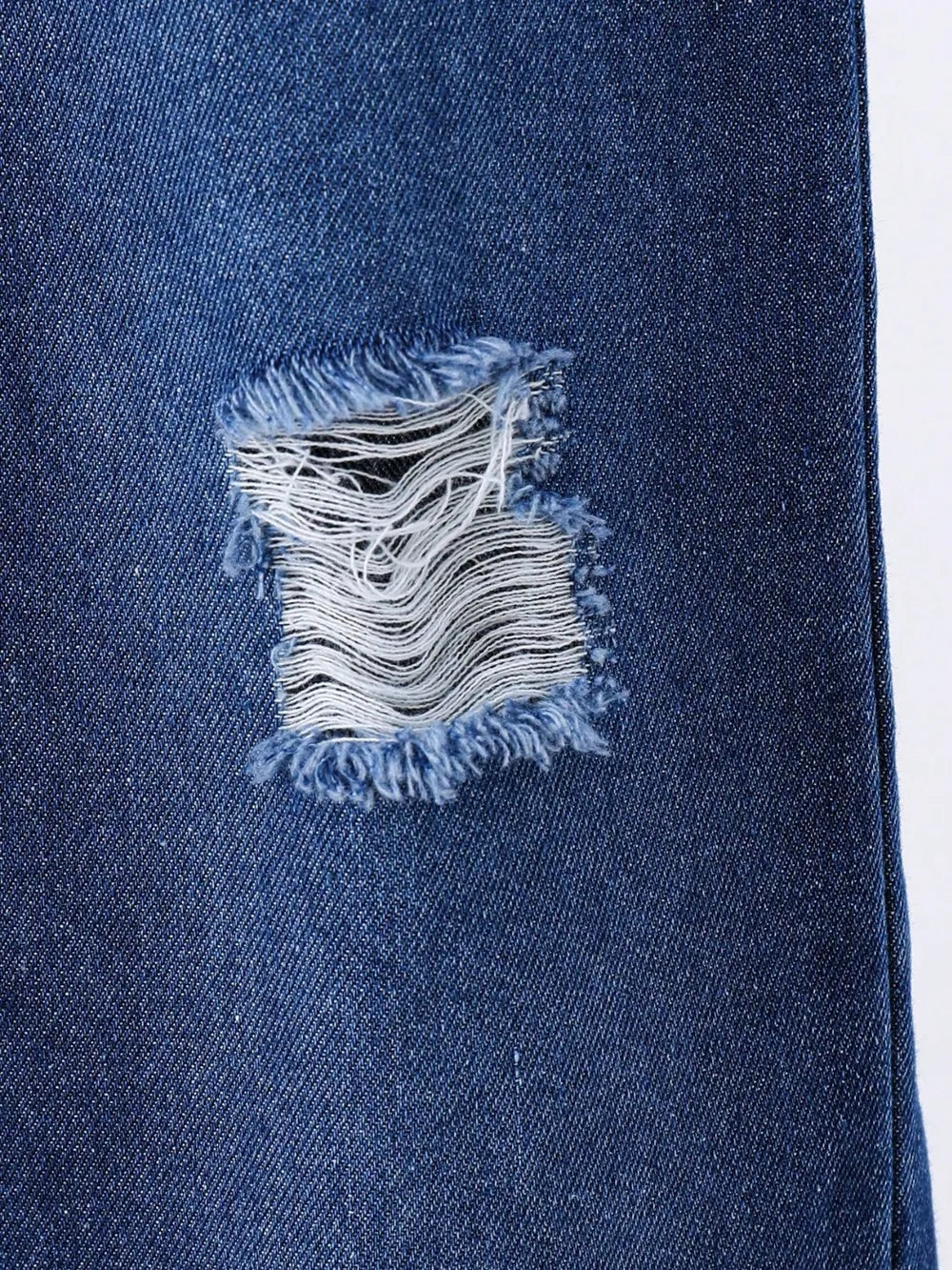 Frayed tear in denim fabric showcasing contrasting blue and white textures.