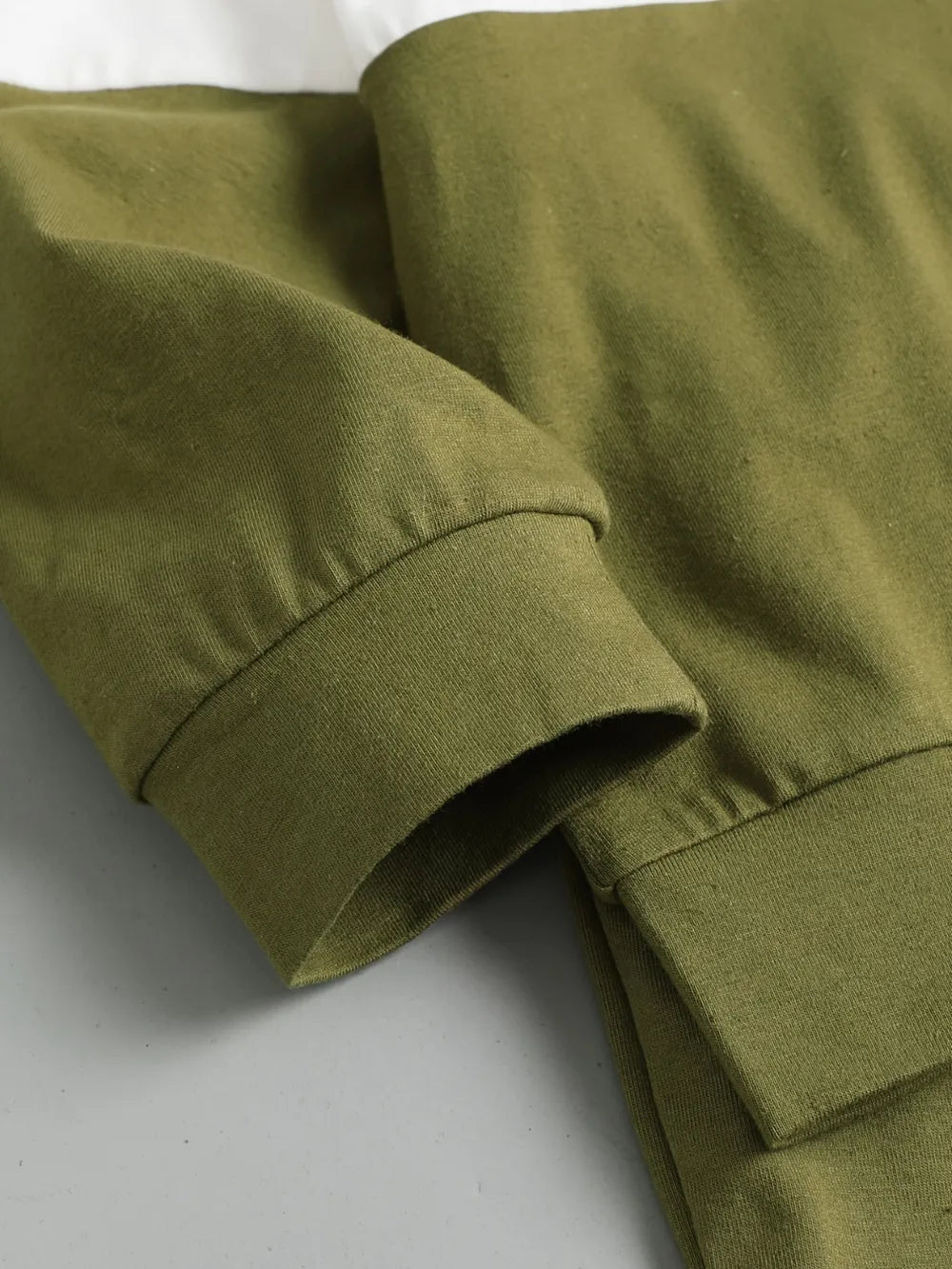 Green cotton fabric with a rolled sleeve and hem detail against a neutral background.