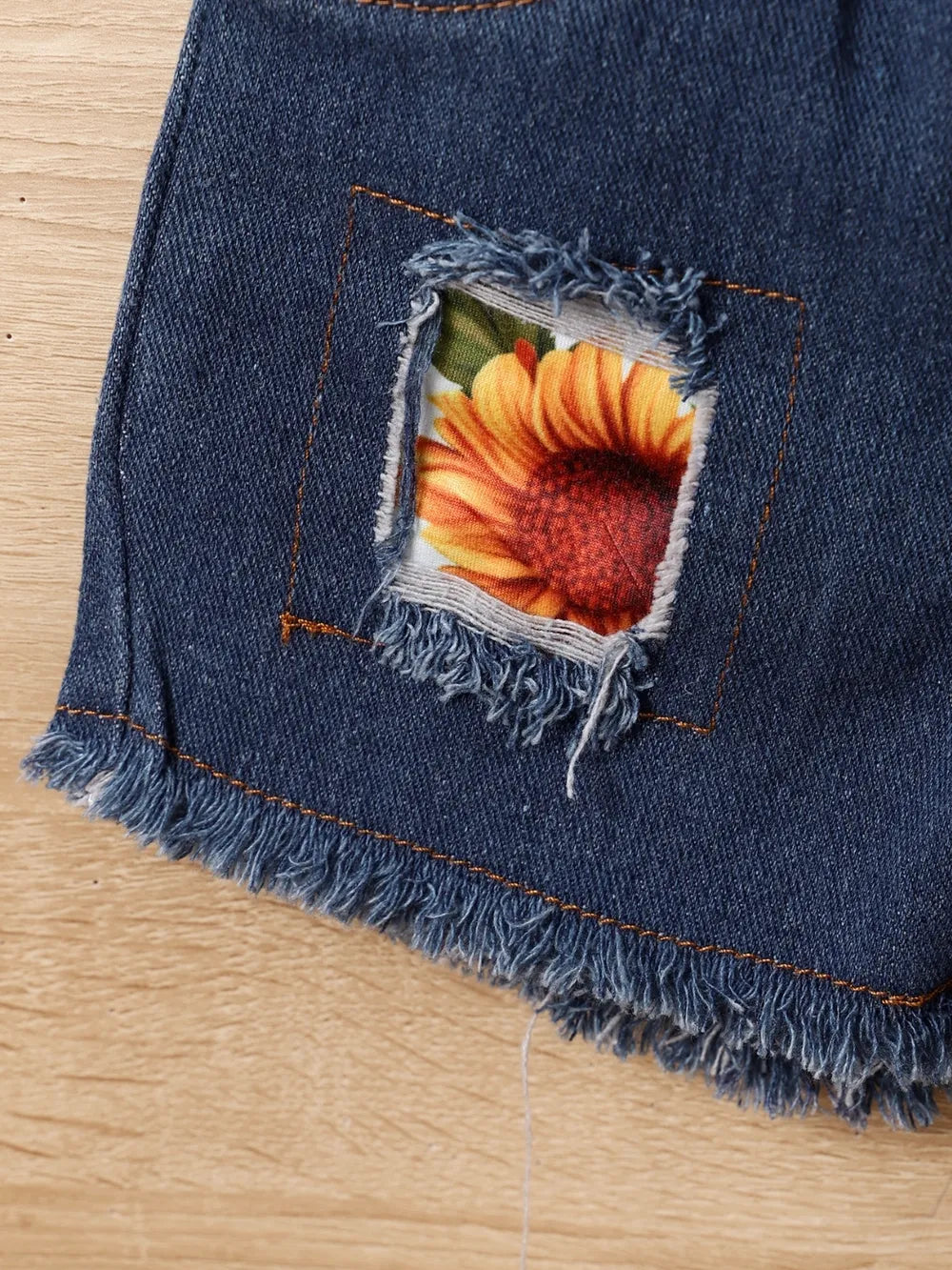 Denim shorts with a frayed patch revealing a sunflower pattern underneath.