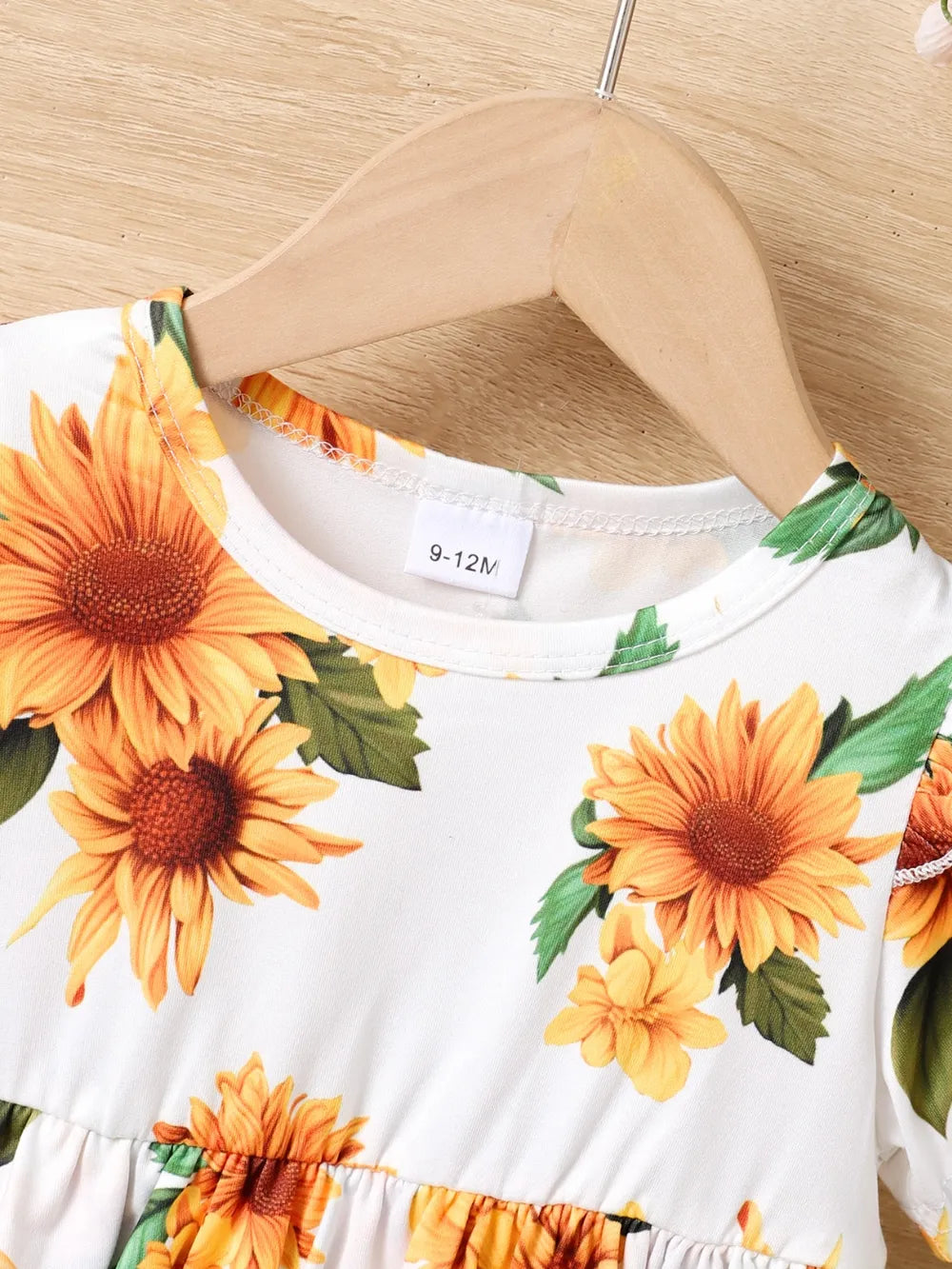 White dress with sunflower pattern, size tag 9-12M, hanging on a wooden hanger.
