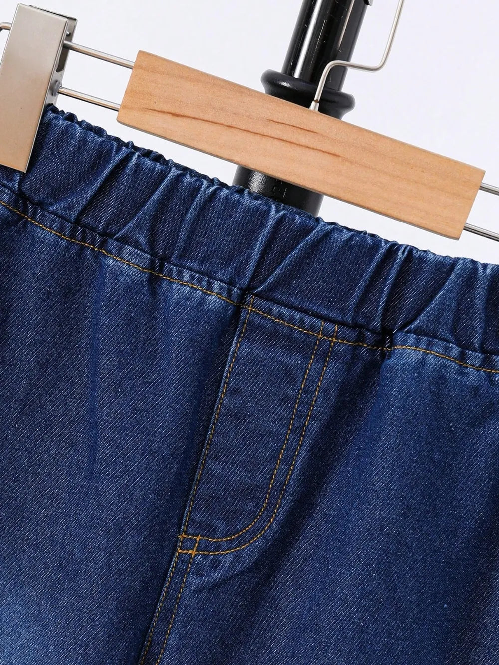Close-up of a pair of blue denim shorts hanging from a wooden clip on a black display stand.