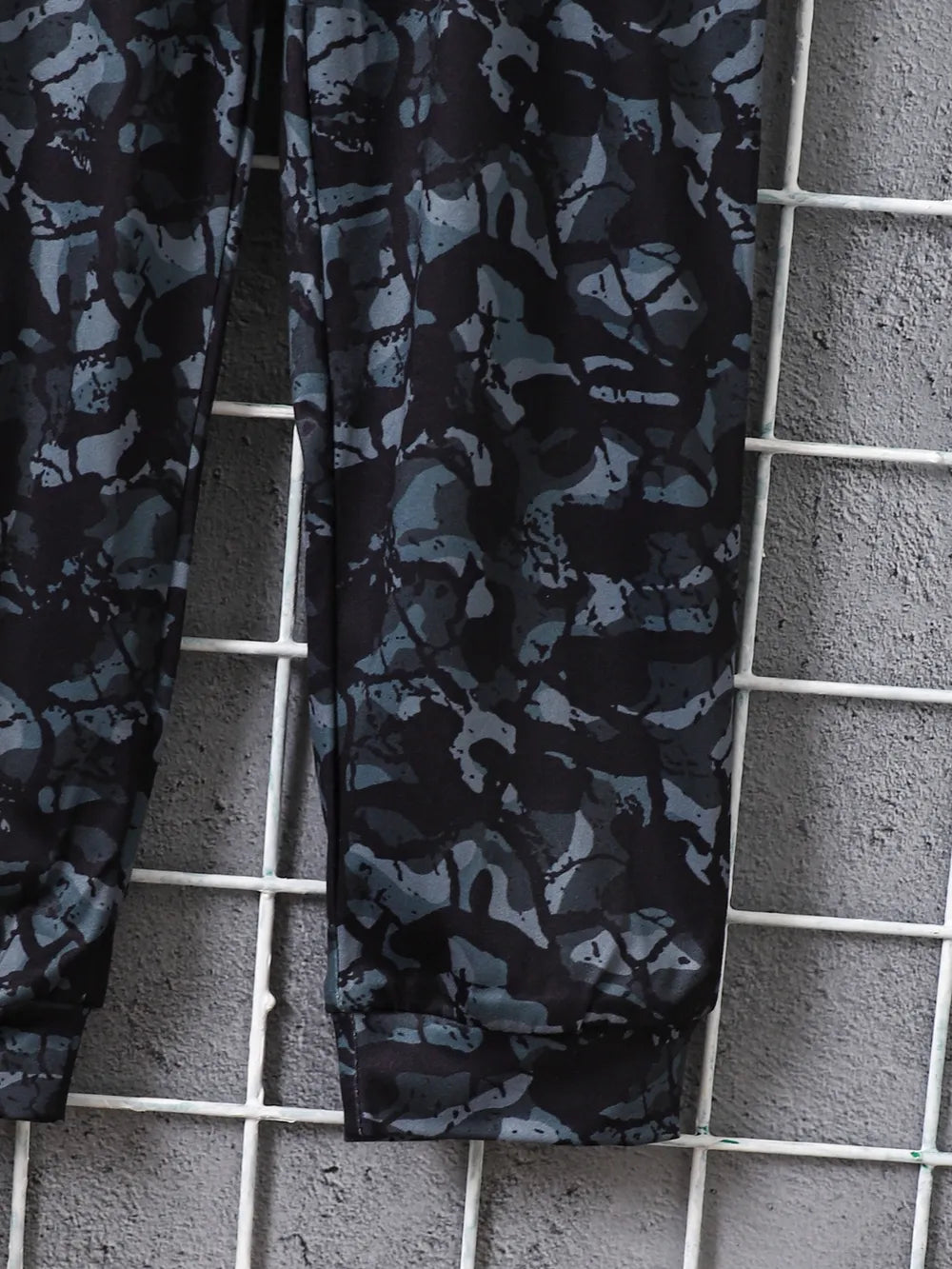 Black athletic leggings with a gray camouflage pattern, displayed against a textured wall.