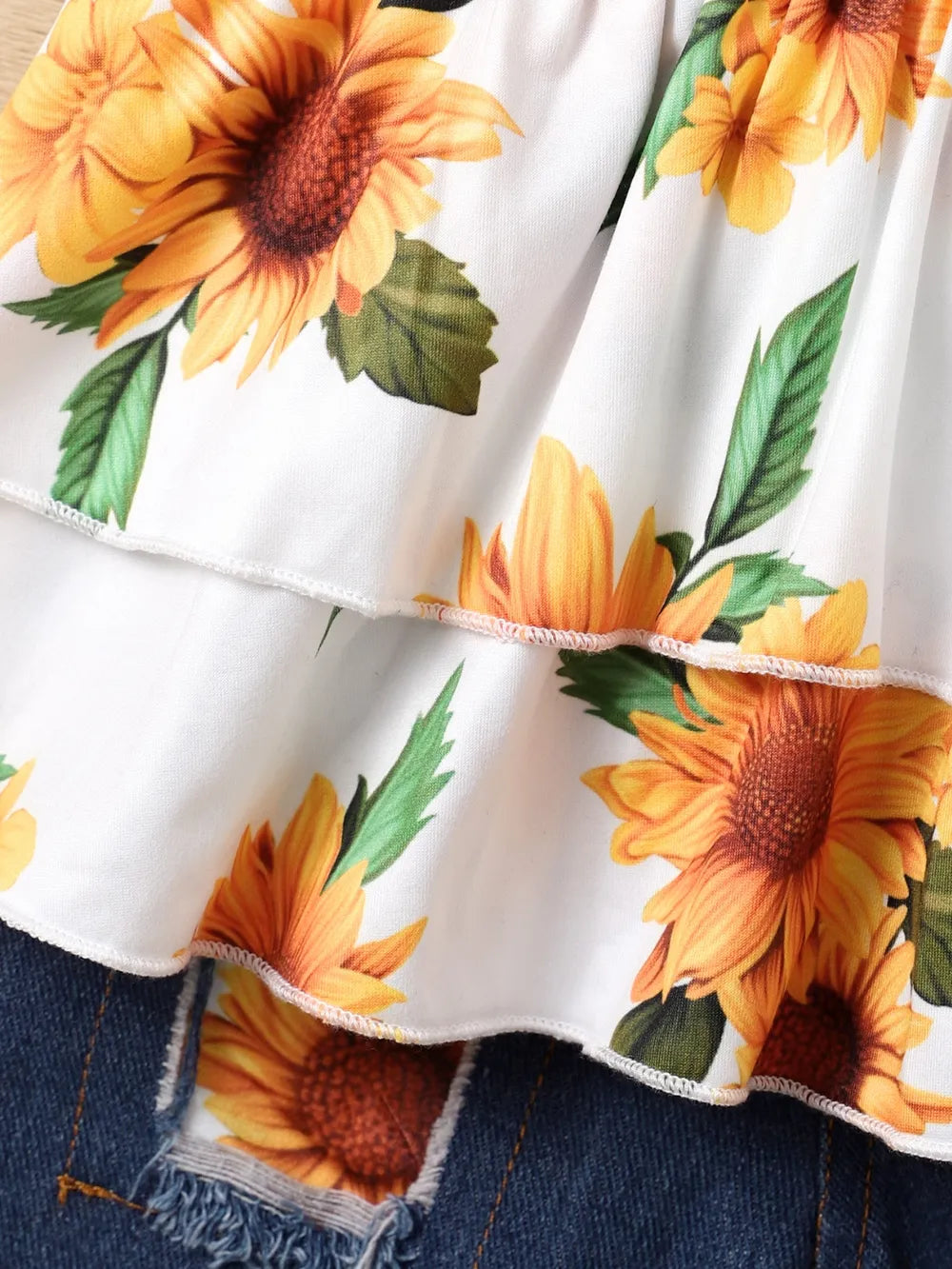 White fabric with vibrant sunflower print layered over denim with frayed edges.