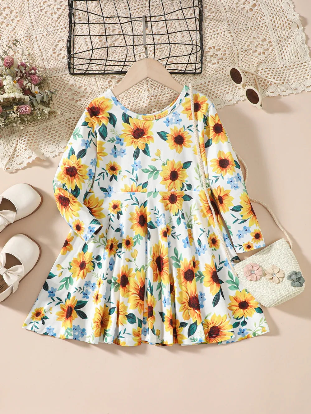 Floral dress with sunflowers, paired with white shoes and a small handbag on lace background.