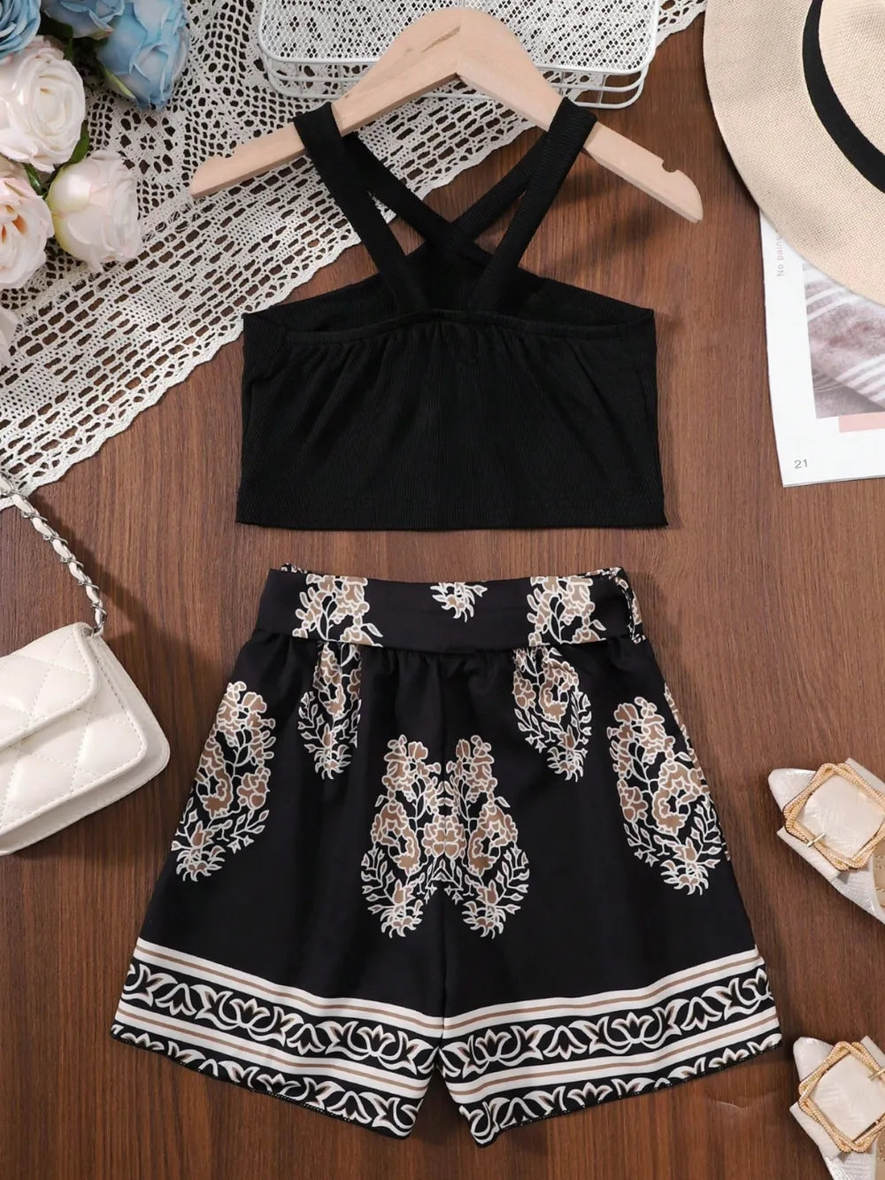 Black cropped top paired with patterned shorts, a handbag, and sandals on a wooden surface.