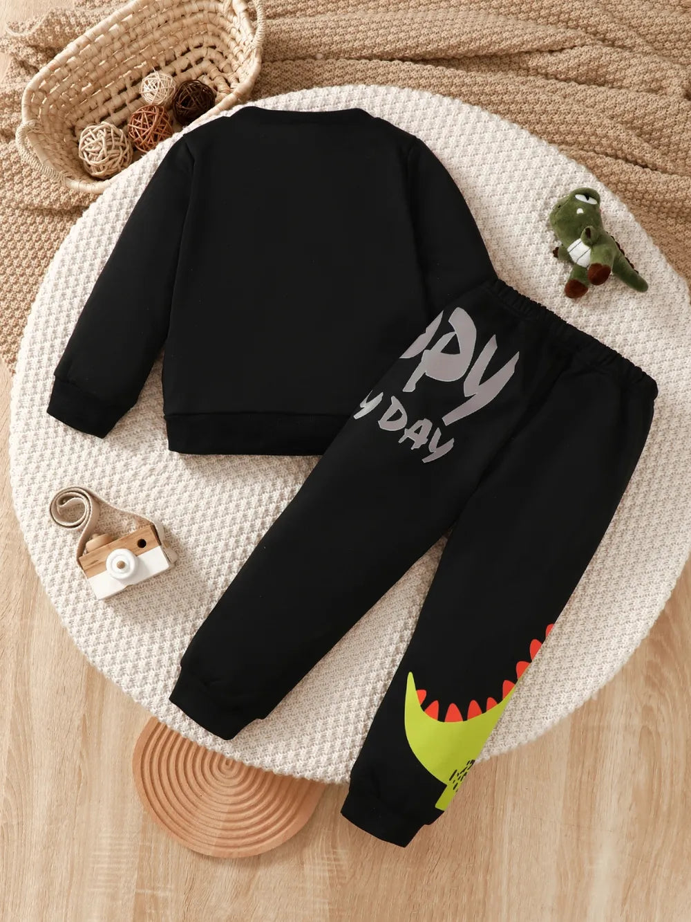 Black children's sweatshirt and pants featuring a dinosaur design, arranged on a round mat.