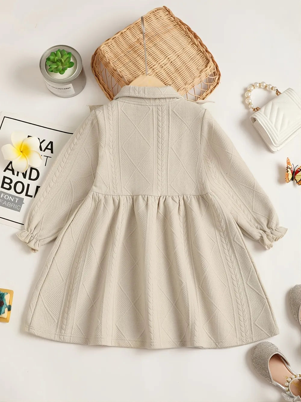 Light beige children's dress with ruffled collar and bow, displayed on a wooden hanger.