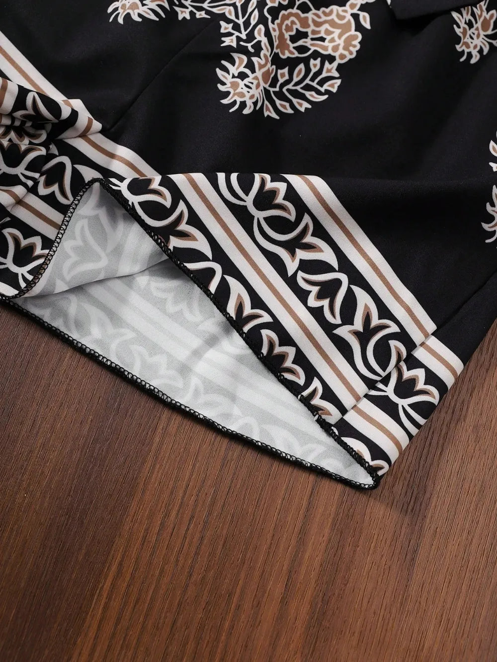 Black fabric with intricate floral patterns and striped accents, laid on a wooden surface.