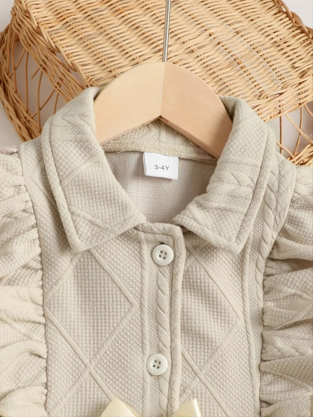 Light beige children's jacket featuring a textured pattern, buttons, and ruffled sleeves.