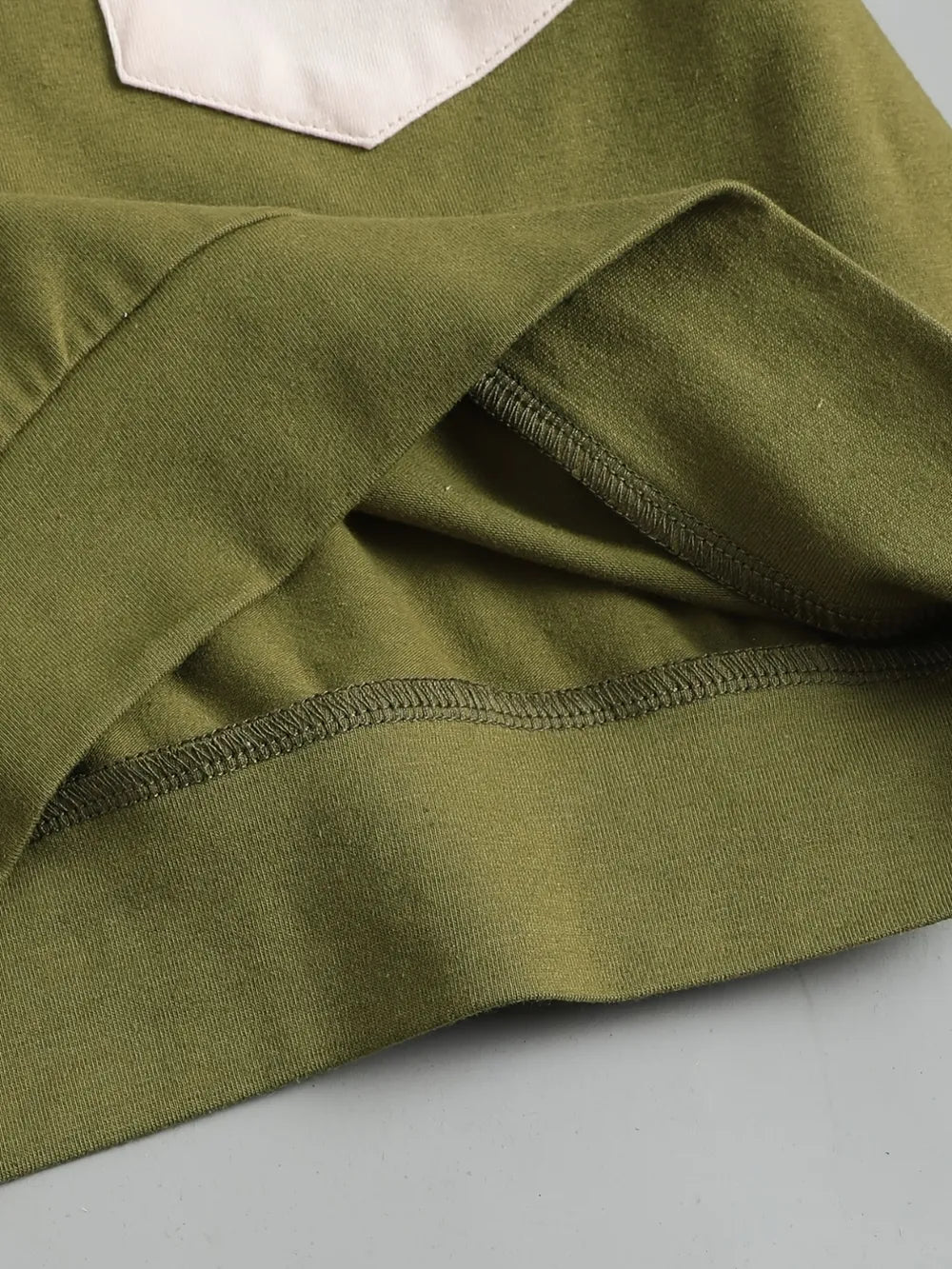 Cotton fabric in olive green with a white pocket detail and visible stitching.