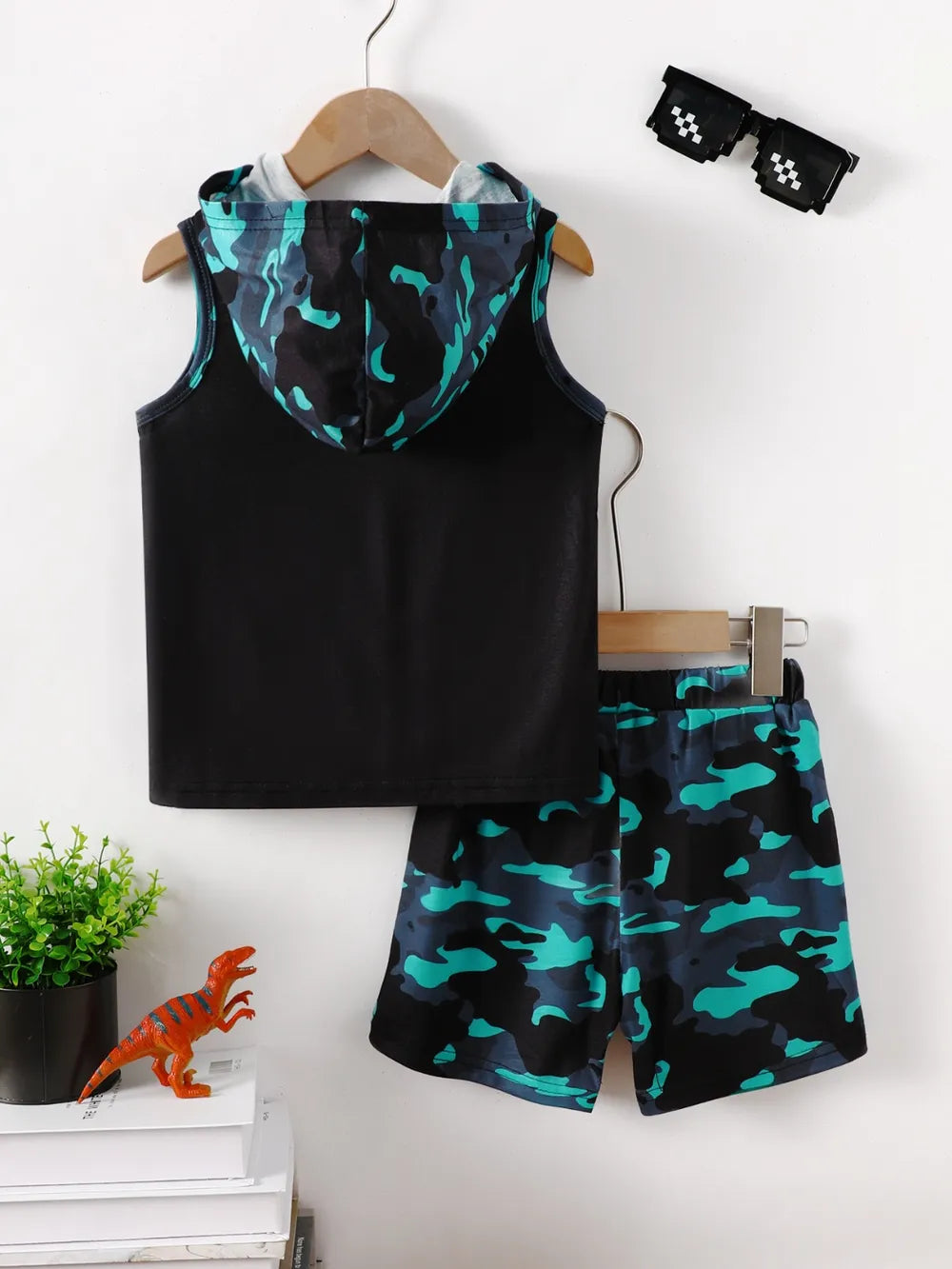 Black sleeveless shirt with a hood, paired with blue camouflage shorts and quirky sunglasses.