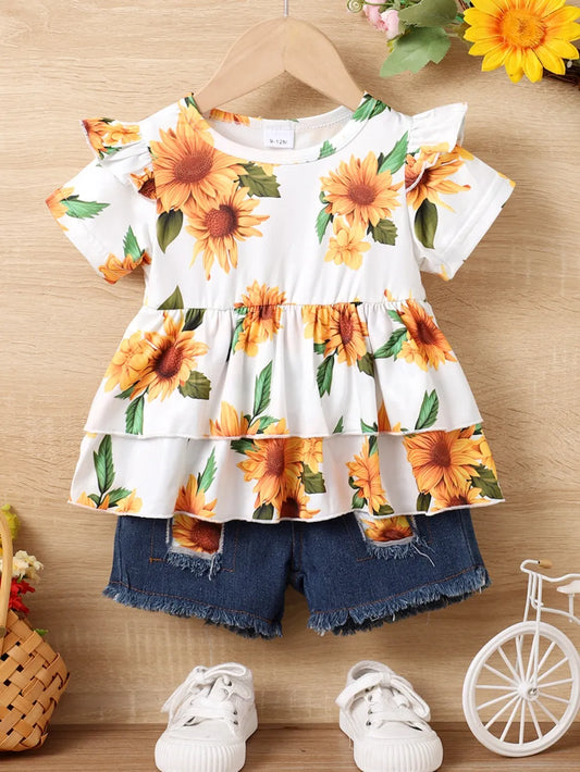 Sunflower-patterned top with denim shorts and white sneakers on a wooden background.