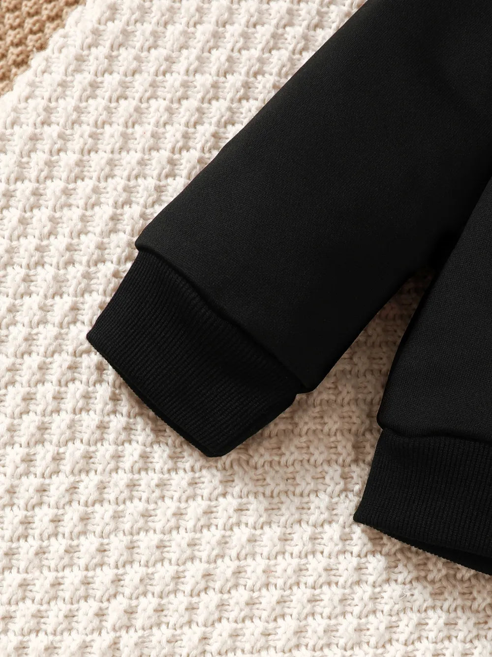 Black sweater sleeve on a textured beige and cream background.