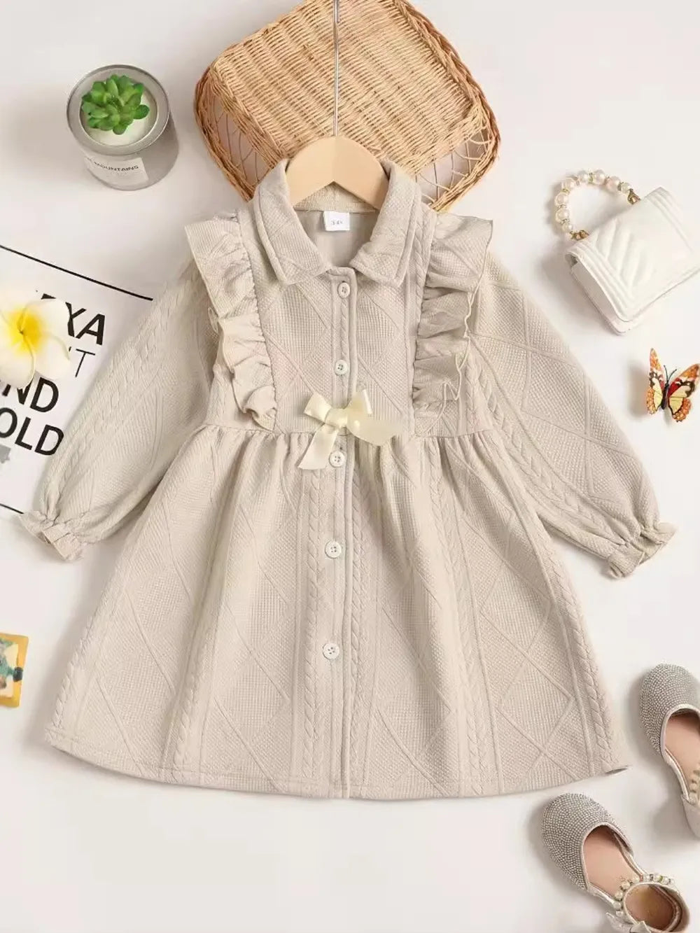 Beige dress with textured pattern, styled flat, accompanied by accessories and a plant.