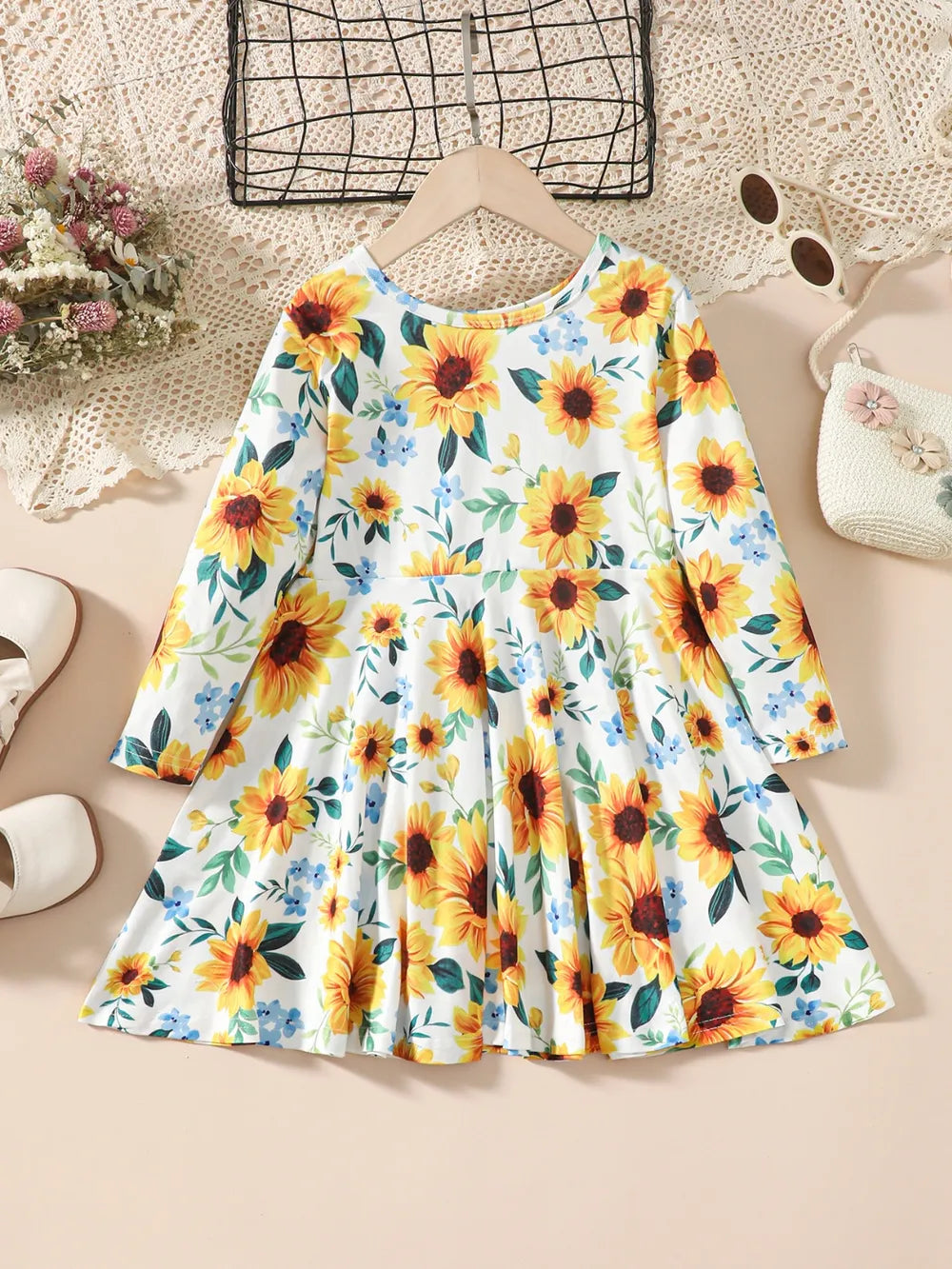 Floral dress with sunflowers and blue flowers, displayed on a hanger against a light background.