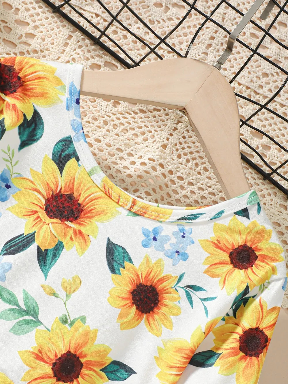 Floral-patterned fabric featuring vibrant sunflowers on a light background, draped over a hanger.