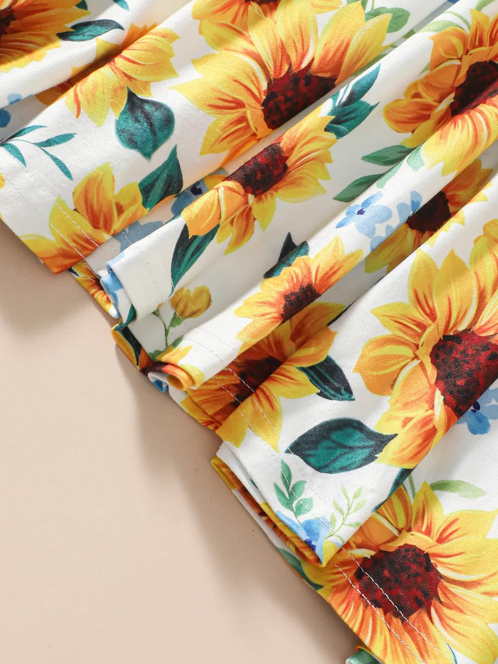 Bright fabric featuring large sunflowers and blue flowers with green leaves against a white background.