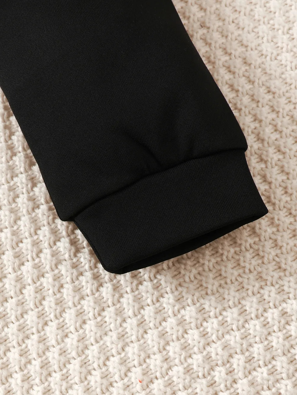Black sleeve cuff resting on a textured, light-colored knitted fabric.