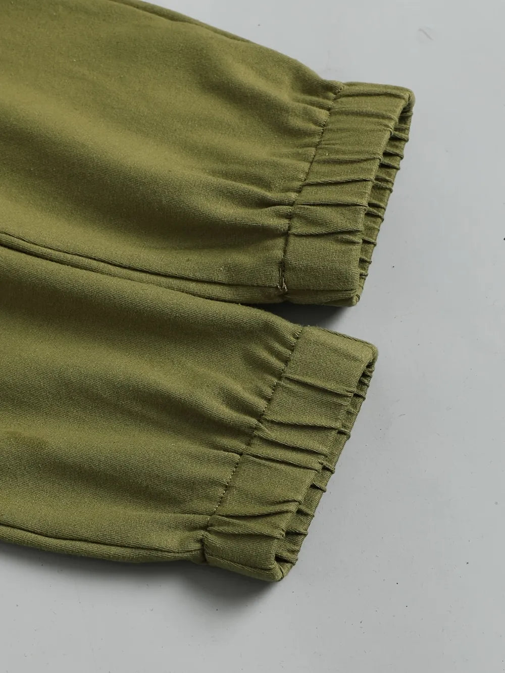 Olive green fabric with gathered elastic cuffs on pants displayed on a flat surface.