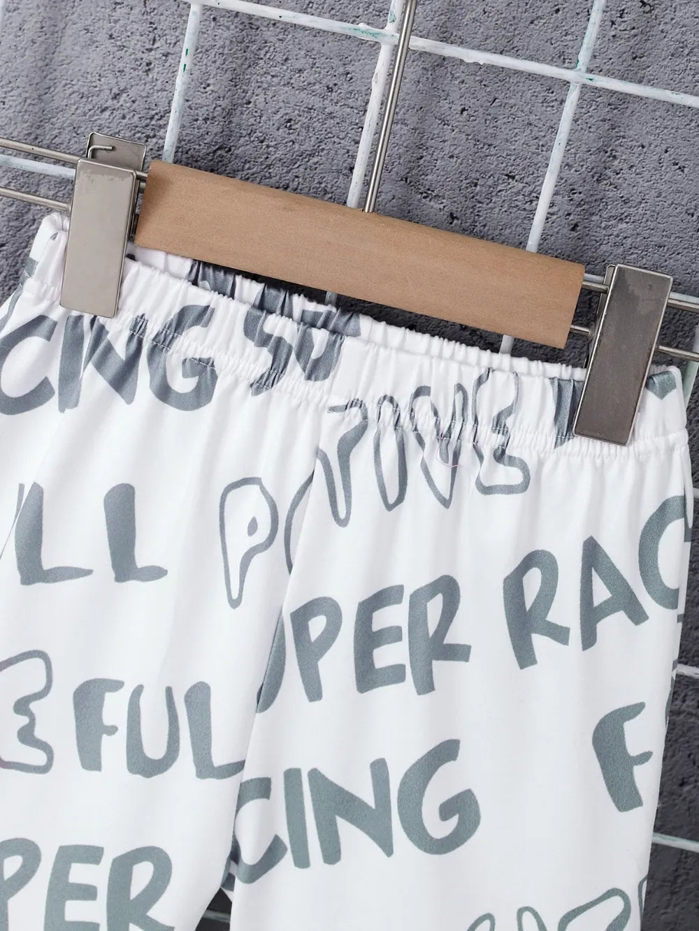 White shorts with playful grey text patterns hang on a metal clothesline against a textured wall.